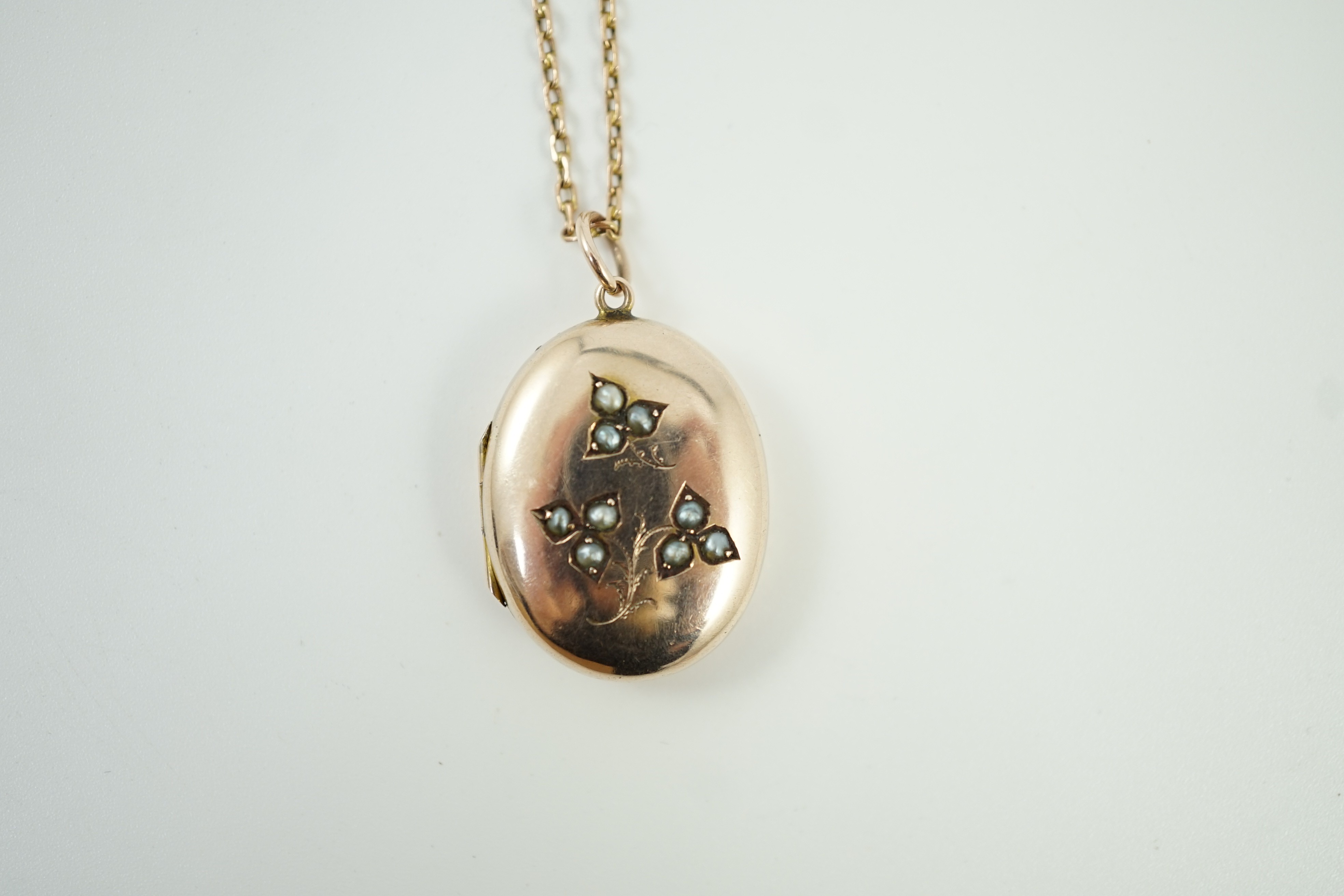 An Edwardian yellow metal and seed pearl set oval locket pendant, 25mm, on a 9ct chain, 47cm, gross weight 9.3 grams.